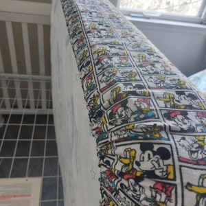 May include: A white fitted crib sheet with a colorful cartoon print featuring Mickey Mouse, Donald Duck, and Goofy. The print is repeated in rows across the sheet.