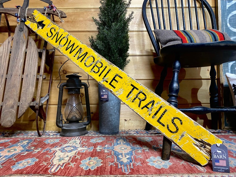 Rustic Snowmobile Trails Directional Sign displayed in a cozy log cabin, hand-painted and distressed for a weathered, vintage look. Perfect for mountain cabins, winter vacation homes, ski lodges, or rustic retreats, this handcrafted sign adds northern trail charm and rustic adventure style. Handmade in Maine with artisan craftsmanship