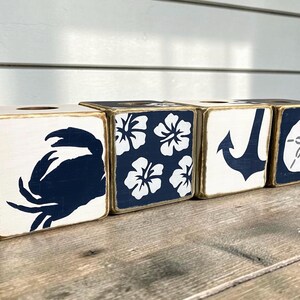 Four coastal tissue boxes with a distressed finish, each featuring a nautical or tropical design in navy blue and white. They display a crab, a hibiscus flower pattern, a ship anchor, and a sand dollar for beach and nautical decor.