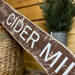 Close-up of the handcrafted Cider Mill wood sign highlighting hand-painted lettering, rich wood grain, layered paint, and vintage distressing inspired by historic apple orchards, country farm signs, and timeless fall decor.