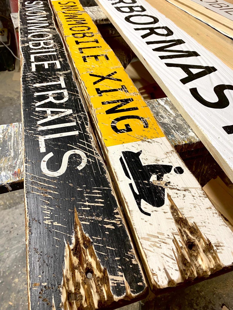Snowmobile Trails Directional Sign displayed in a Maine workshop, showing the hand-painting and artisan distressing process. Perfect for rustic cabins, lodges, or winter vacation homes, highlighting northern trail life and cozy alpine-inspired décor.
