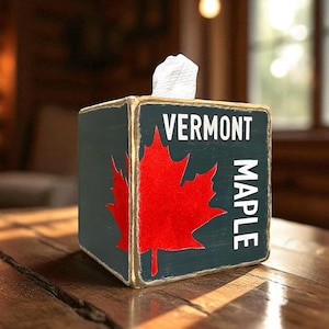 May include: A wooden tissue box with a red maple leaf design and the words "VERMONT MAPLE" in white. The box is dark green with gold trim and sits on a wooden table.