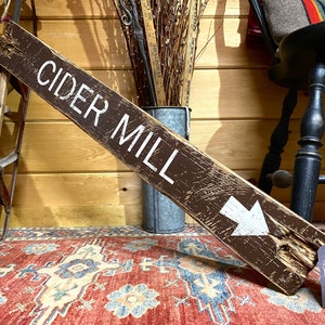 Handcrafted Cider Mill wood sign displayed inside a cozy log cabin, bringing the warmth of apple orchard traditions, autumn harvest, rustic lodge style, and timeless fall cabin decor to your favorite gathering space.