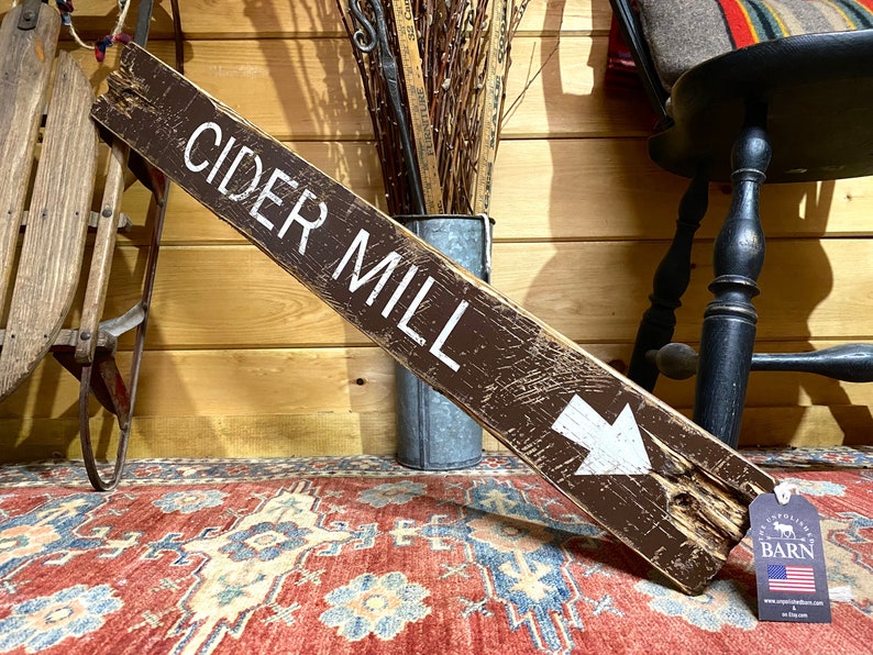 Handcrafted Cider Mill wood sign displayed inside a cozy log cabin, bringing the warmth of apple orchard traditions, autumn harvest, rustic lodge style, and timeless fall cabin decor to your favorite gathering space.