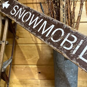 Close-up of hand-painted lettering on a Snowmobile Trails Directional Sign, highlighting the detailed craftsmanship, weathered rustic finish, and northern trail-inspired design, ideal for cabins, lodges, or winter vacation homes