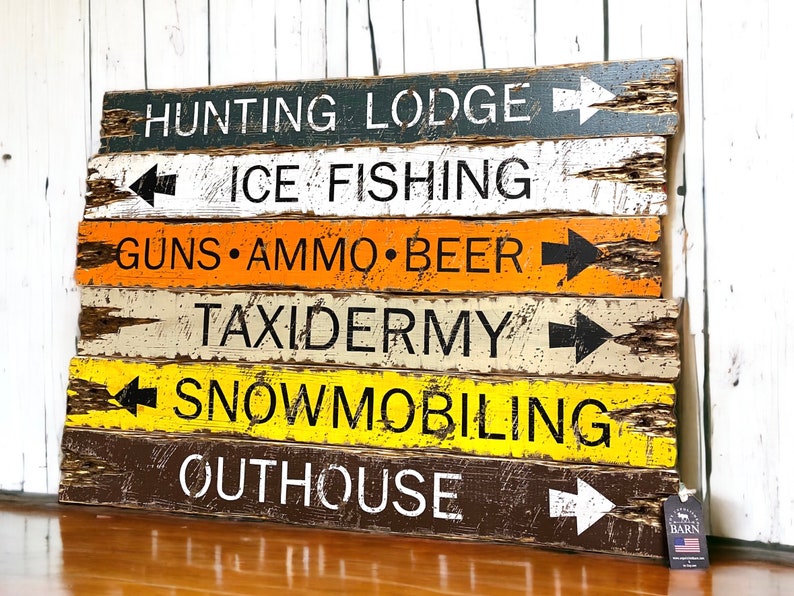 Puede incluir: Un letrero de madera r&uacute;stico con flechas direccionales y texto. El letrero presenta varios destinos como "Hunting Lodge", "Ice Fishing" y "Guns &bull; Ammo &bull; Beer". El letrero tiene un acabado envejecido con una mezcla de colores que incluyen negro, blanco, naranja y amarillo.