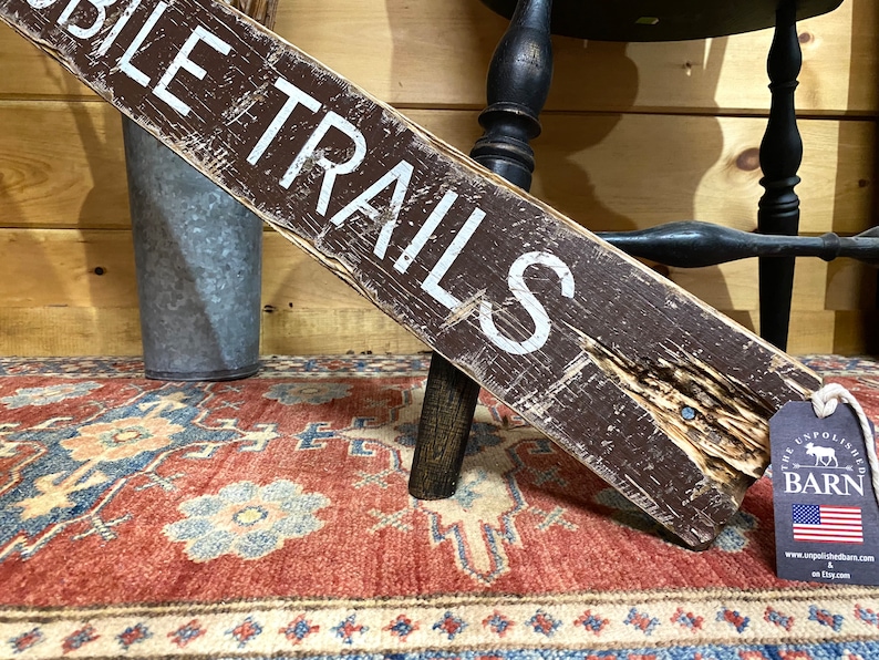 Close-up of a handcrafted Snowmobile Trails Sign, highlighting the weathered, distressed finish and hand-painted lettering. Ideal for rustic cabins, lodges, or winter vacation homes, showcasing northern trail charm and alpine-inspired décor