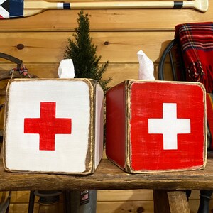 Rustic First Aid wood tissue box cover displayed in a ski cabin or lodge-style bathroom, perfect for beach houses, poolside spaces, cabins, and guest rooms. Handcrafted from wood with natural texture, this piece brings nostalgic ski and lifeguard-inspired charm to everyday décor.