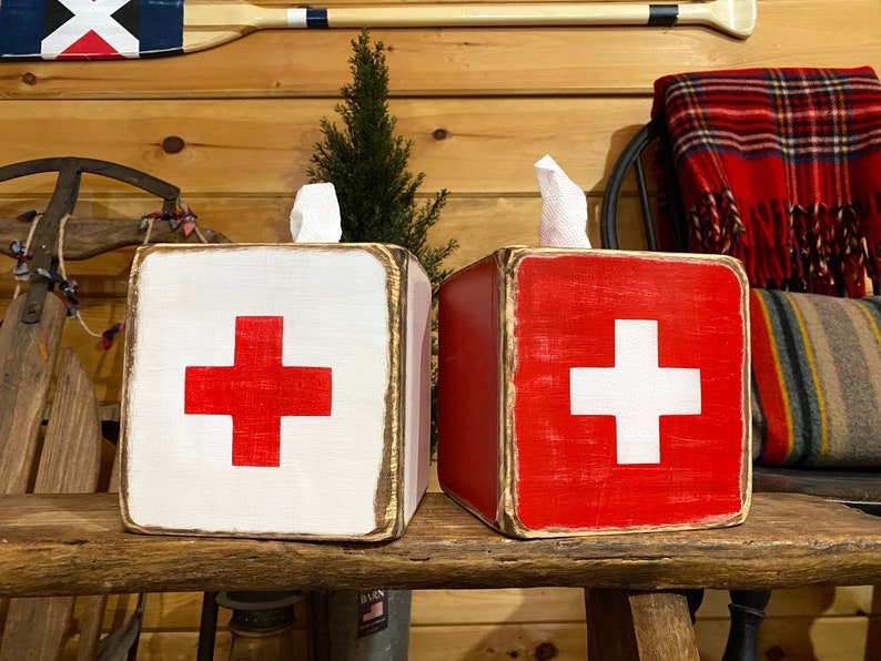 Rustic First Aid wood tissue box cover displayed in a ski cabin or lodge-style bathroom, perfect for beach houses, poolside spaces, cabins, and guest rooms. Handcrafted from wood with natural texture, this piece brings nostalgic ski and lifeguard-inspired charm to everyday décor.