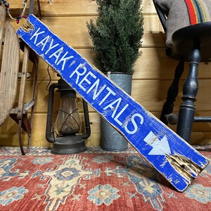 Kayak Rentals wood sign angled view, rustic handcrafted wall décor ideal for vacation rentals, beach houses, lake cabins, and coastal cottages, celebrating outdoor and water adventure lifestyle