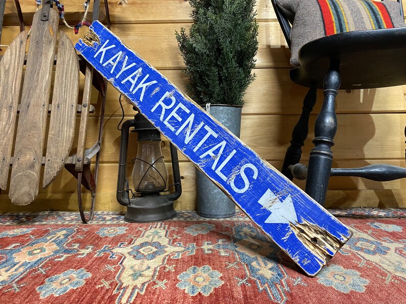Kayak Rentals wood sign angled view, rustic handcrafted wall décor ideal for vacation rentals, beach houses, lake cabins, and coastal cottages, celebrating outdoor and water adventure lifestyle
