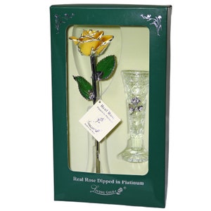 May include: A single yellow rose dipped in platinum, preserved in a clear glass vase. The rose and vase are displayed in a green box with the words "Real Rose Dipped in Platinum" and "Living Gold!" printed on the front.