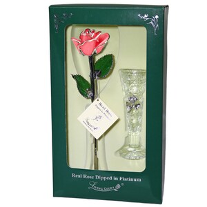 May include: A single pink rose dipped in platinum, preserved in a clear glass vase. The rose and vase are displayed in a green box with the words "Real Rose Dipped in Platinum" and "Living Gold" printed on the box.