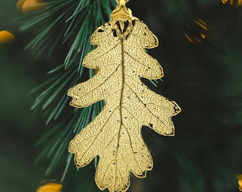 May include: A gold leaf ornament shaped like an oak leaf. The leaf is delicate and intricate, with visible veins. The ornament is hanging from a gold string.