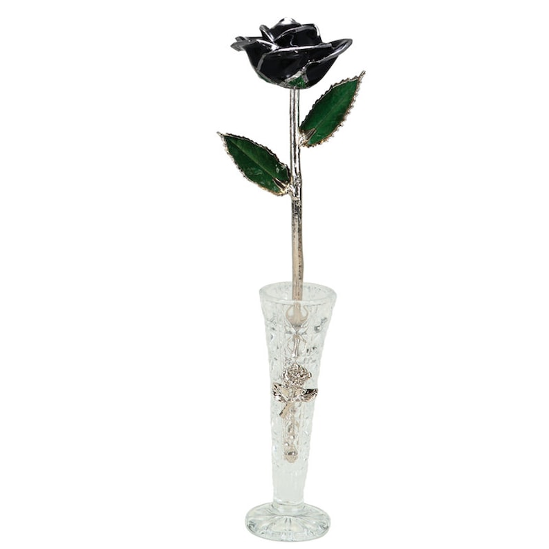 May include: A single black rose with green leaves is displayed in a clear glass vase. The rose is made of metal and has a silver finish.