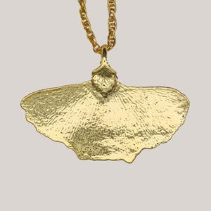 May include: A gold-colored pendant necklace featuring a textured ginkgo leaf design. The pendant is suspended from a matching gold chain. The leaf has detailed veining and a slightly irregular edge, giving it a naturalistic appearance. The necklace is suitable for everyday wear.
