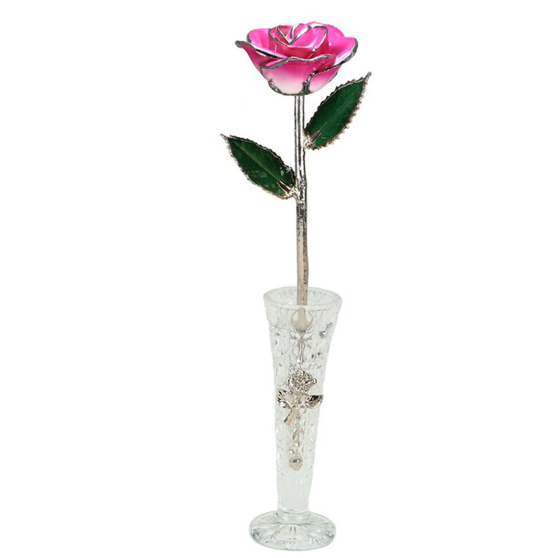 May include: A single, pink, metallic rose with green leaves is displayed in a clear glass vase with a cut-glass design.