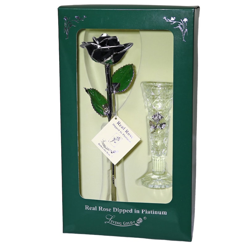 May include: A single black rose dipped in platinum, preserved in a clear glass vase. The rose and vase are displayed in a green box with the text "Real Rose Dipped in Platinum" and "Living Gold!"