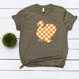 May include: A green t-shirt with a white and orange gingham turkey graphic.