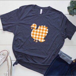 May include: A navy blue t-shirt with a white and orange gingham turkey design.