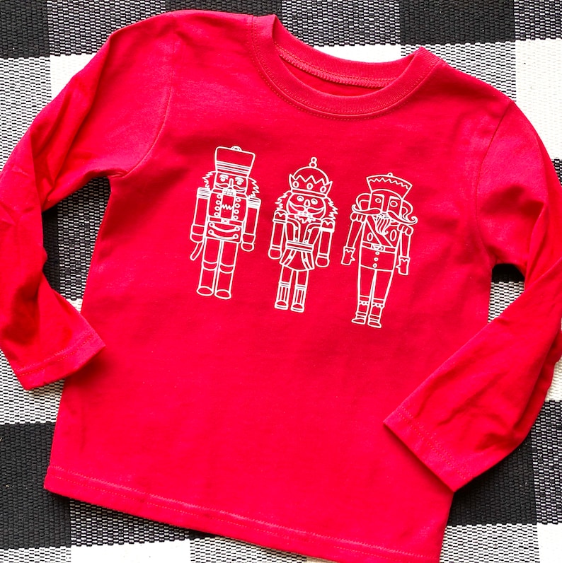 May include: Red long-sleeved shirt with a white outline of three nutcracker figures.