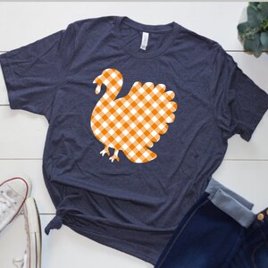 May include: A navy blue t-shirt with a white and orange gingham turkey design.