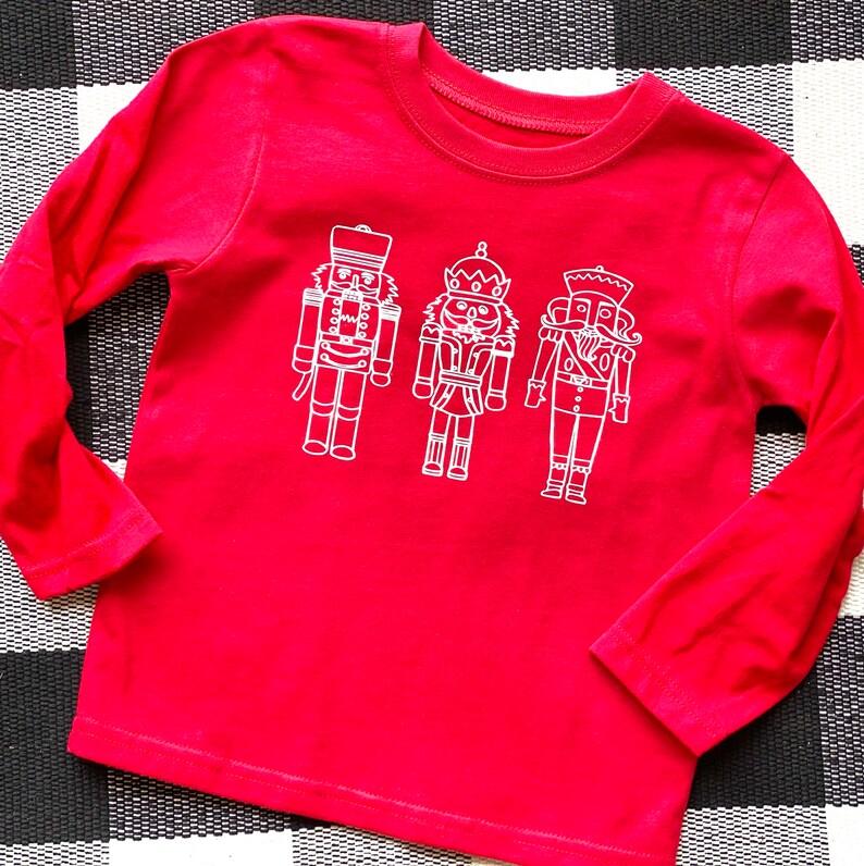 May include: Red long-sleeved shirt with a white outline of three nutcracker figures.
