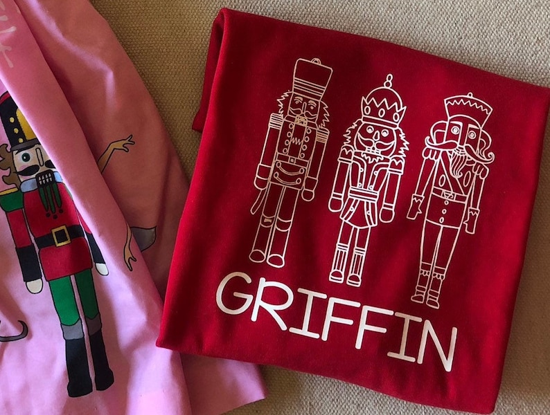 May include: Red t-shirt with a white design of three nutcracker figures and the name "GRIFFIN" printed below.