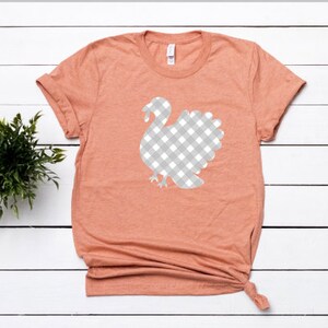 May include: A peach colored t-shirt with a white and gray gingham turkey design.