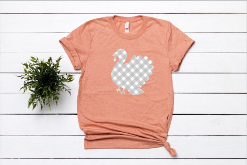 May include: A peach colored t-shirt with a white and gray gingham turkey design.