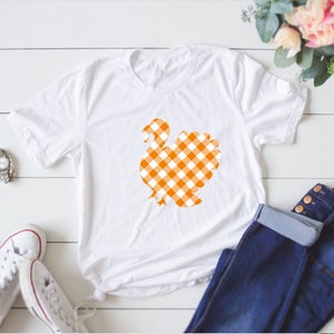 May include: White t-shirt with an orange and white gingham turkey design.