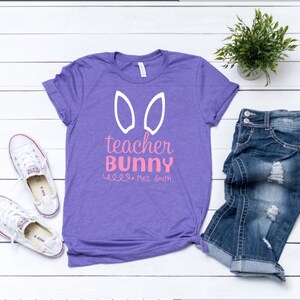 May include: Purple t-shirt with white bunny ears and the text "teacher bunny" in pink with the name "Mrs. Smith" underneath.