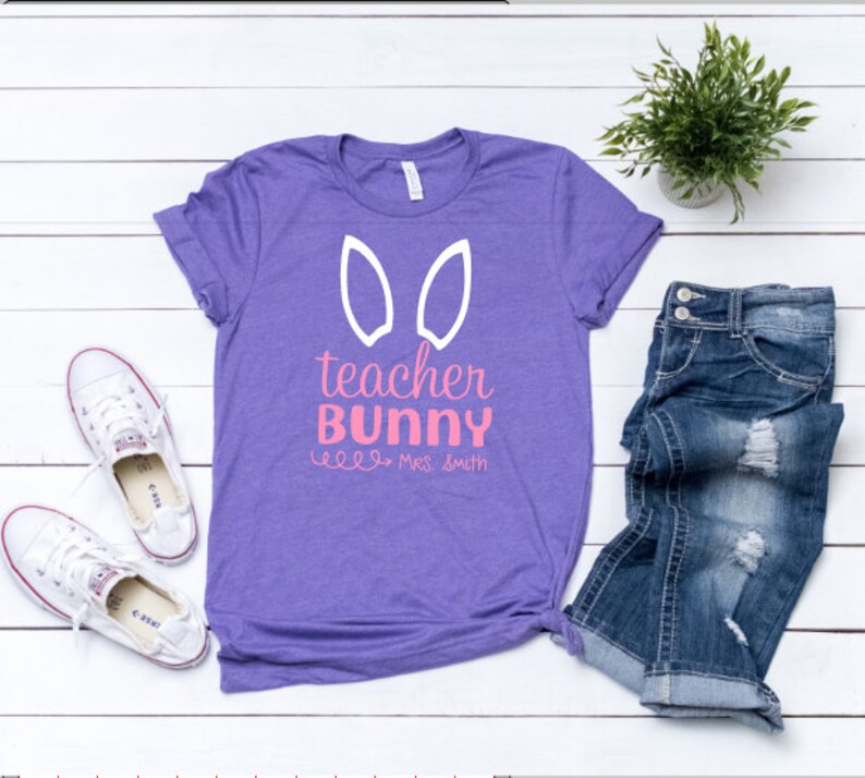 May include: Purple t-shirt with white bunny ears and the text "teacher bunny" in pink with the name "Mrs. Smith" underneath.