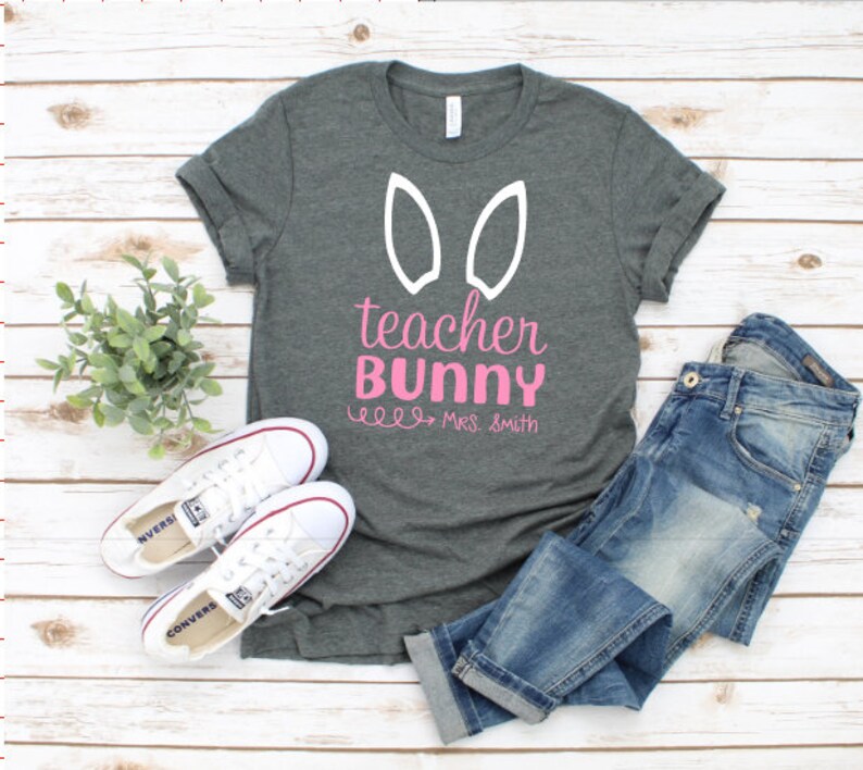 May include: A gray t-shirt with white bunny ears and the text "teacher bunny" in pink lettering. The text "Mrs. Smith" is also included in pink lettering.
