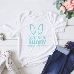 May include: White t-shirt with a turquoise bunny ear design and the text "teacher bunny" and "Mrs. Smith".