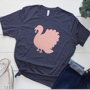 May include: A navy blue t-shirt with a pink glitter turkey graphic.