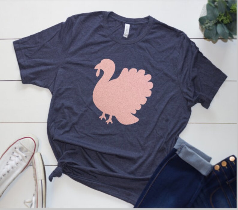 May include: A navy blue t-shirt with a pink glitter turkey graphic.