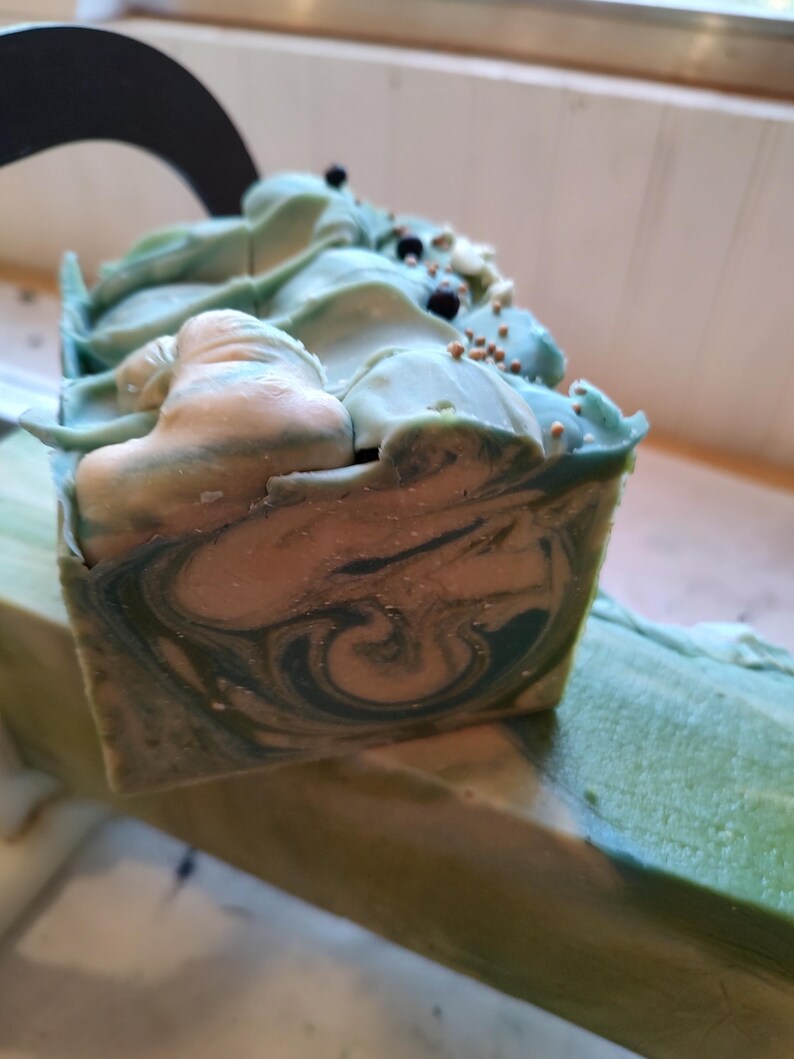 Pu&ograve; includere: Una saponetta fatta a mano con un motivo a spirale di verde, blu e bianco. Il sapone &egrave; decorato con granelli neri e dorati.