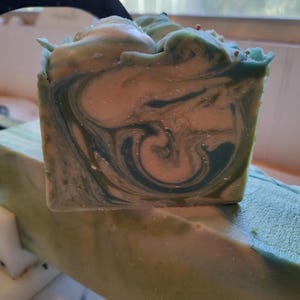 Pu&ograve; includere: Una saponetta fatta a mano con un motivo a spirale in tonalit&agrave; di verde e bianco. Il sapone ha un aspetto maculato con piccole macchie di colore in tutto.