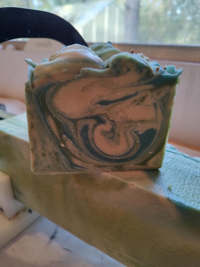 Pu&ograve; includere: Una saponetta fatta a mano con un motivo a spirale in tonalit&agrave; di verde e bianco. Il sapone ha un aspetto maculato con piccole macchie di colore in tutto.