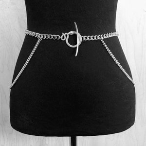 May include: A silver chain belt with a snake-shaped clasp. The chain is made of small, linked circles and has a long, dangling chain on each side.