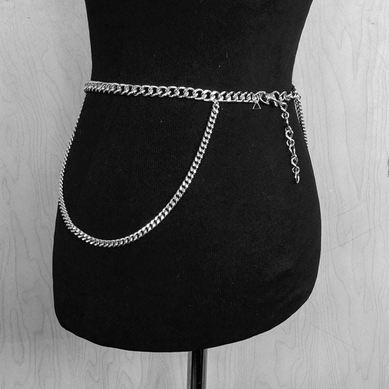 May include: A silver chain belt with a double layer of chain. The chain is thick and has a chunky link design. The belt is worn around the waist of a mannequin.