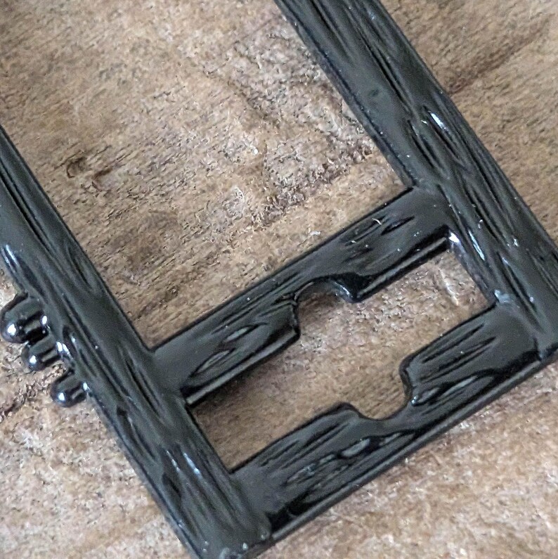 May include: Close-up of a black, rectangular frame with a textured, wood-like appearance. The frame has a glossy finish and features rounded edges and a unique cutout design. The frame is likely for a picture or artwork.