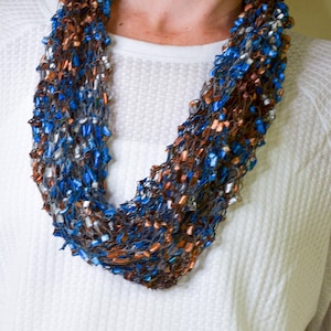 May include: A brown, blue, and white infinity scarf made of yarn. The scarf is made of a soft, lightweight material and is perfect for layering.