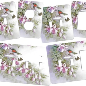 May include: A set of light switch and outlet covers featuring a hummingbird in flight with pink flowers. The covers are white with a watercolor-style design.