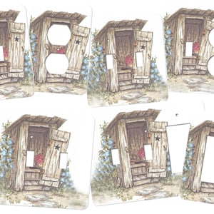 May include: Set of five light switch and outlet covers featuring a rustic outhouse design. The covers are printed with a detailed illustration of a wooden outhouse with a star on the door, surrounded by blue flowers. The outhouse is set against a white background.