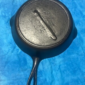 May include: A black cast iron skillet with a long handle. The skillet has a smooth surface and a small, round hole in the handle.