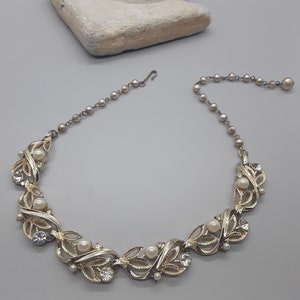 Puede incluir: Un collar de tono dorado con una cadena delicada y un diseño de hojas y perlas falsas. El collar tiene un cierre de gancho.