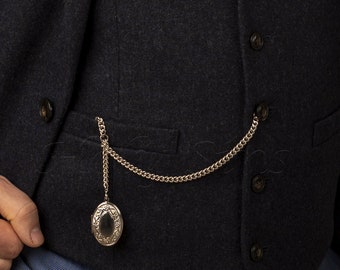 Può includere: Un orologio da tasca d'argento con una catena attaccata a un gilet blu scuro.