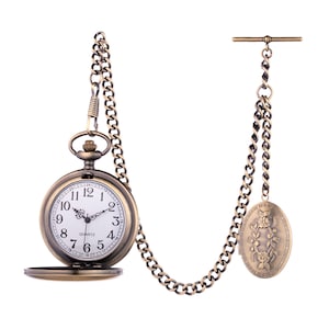 Può includere: Un orologio da tasca in stile vintage con quadrante bianco e lancette nere. L'orologio ha una finitura dorata ed è attaccato a una catena con un ciondolo decorativo.